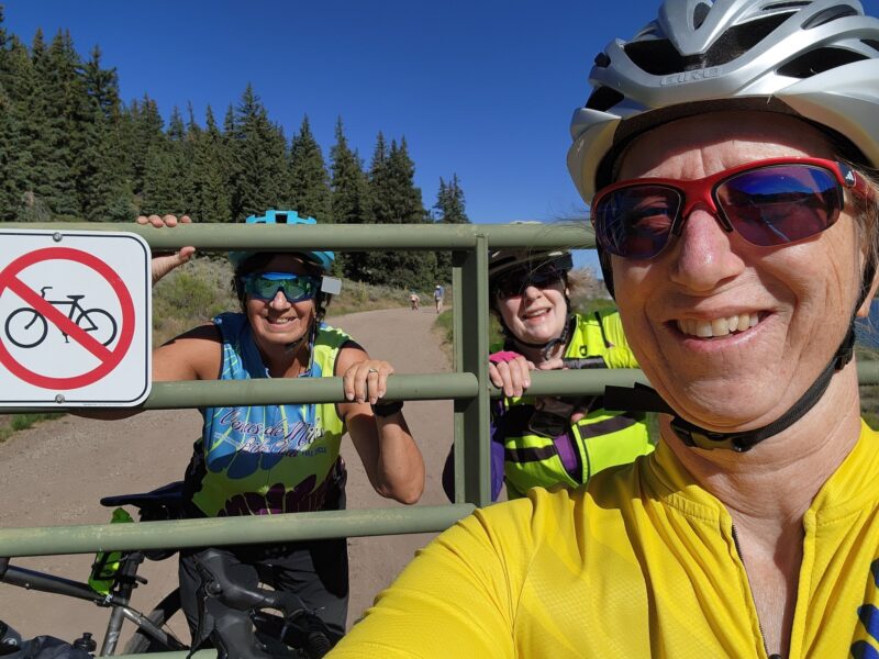 Three Venus members taking a selfie in front of a gate with a no bicycling sign